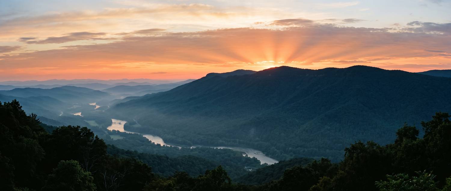 El sol se pone detrás de una montaña boscosa sobre un valle con neblina